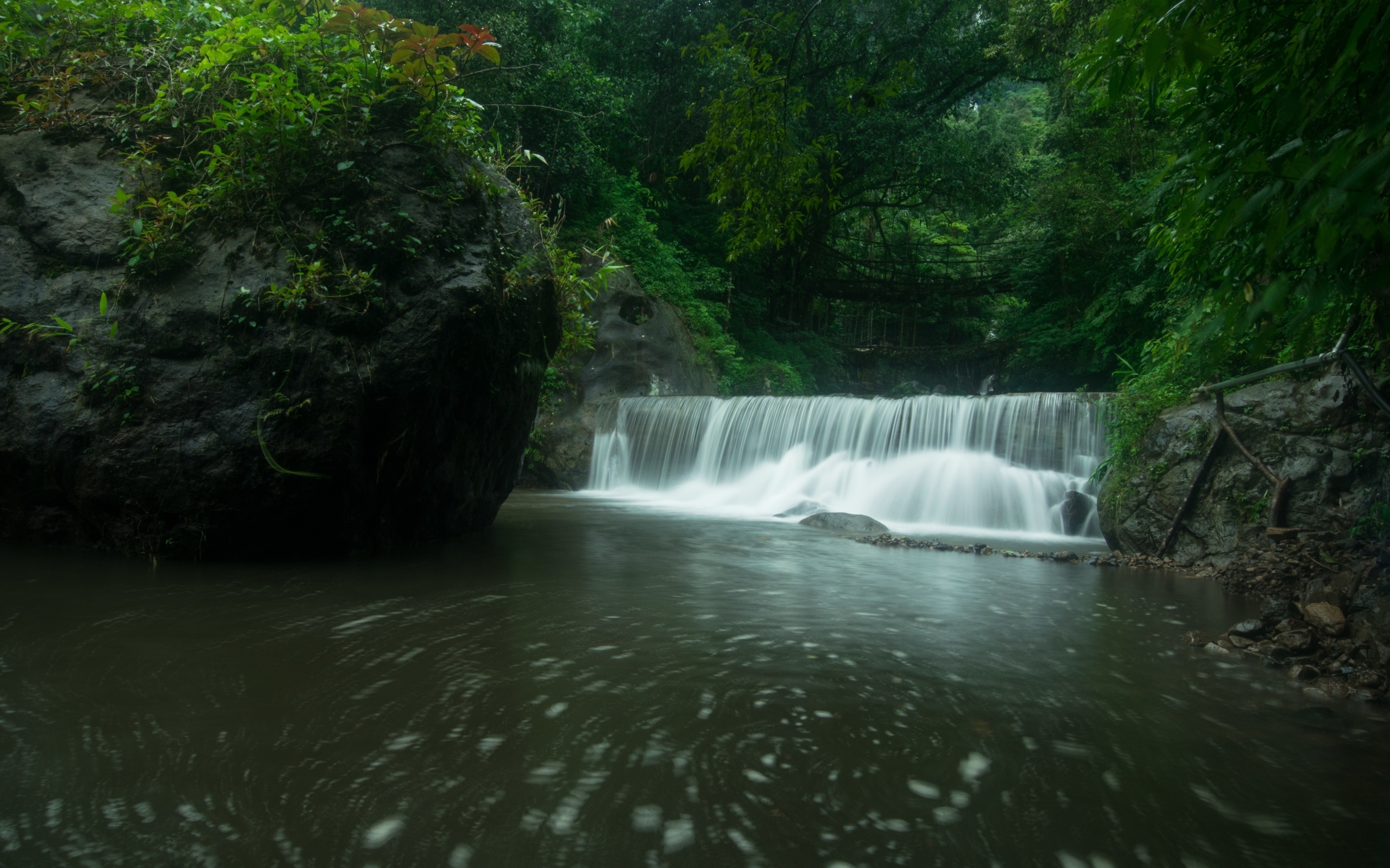 Водопад стекает в реку с большими камнями в лесу