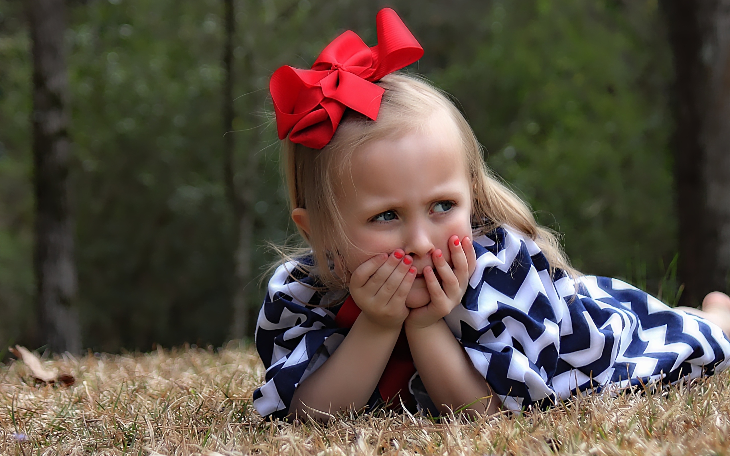Маленькая девочка с красным бантом на голове лежит на траве