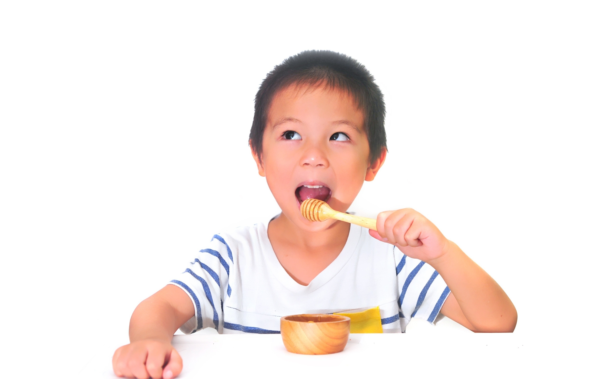 Мальчик азиат ест мед на сером фоне