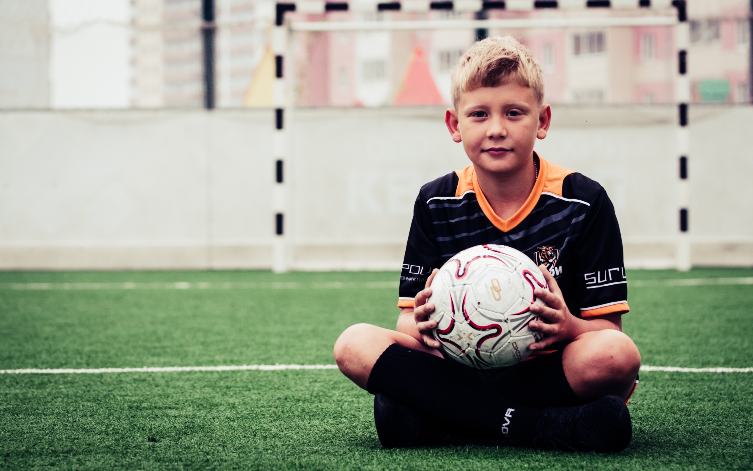 Мальчик футболист сидит на траве с мячом