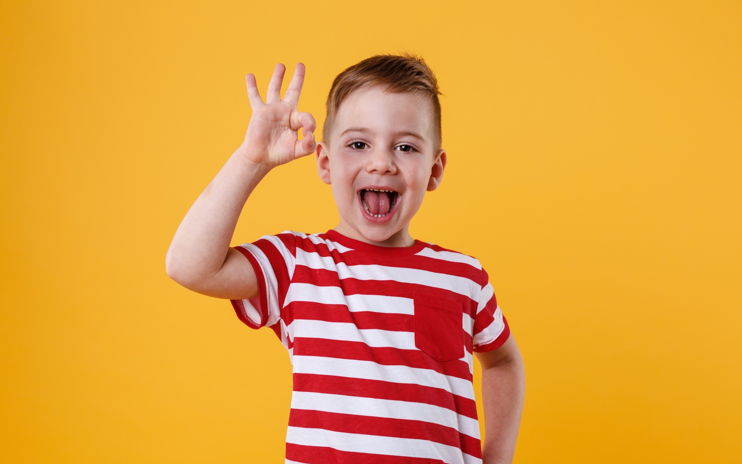 Веселый мальчик в полосатой футболке на оранжевом фоне