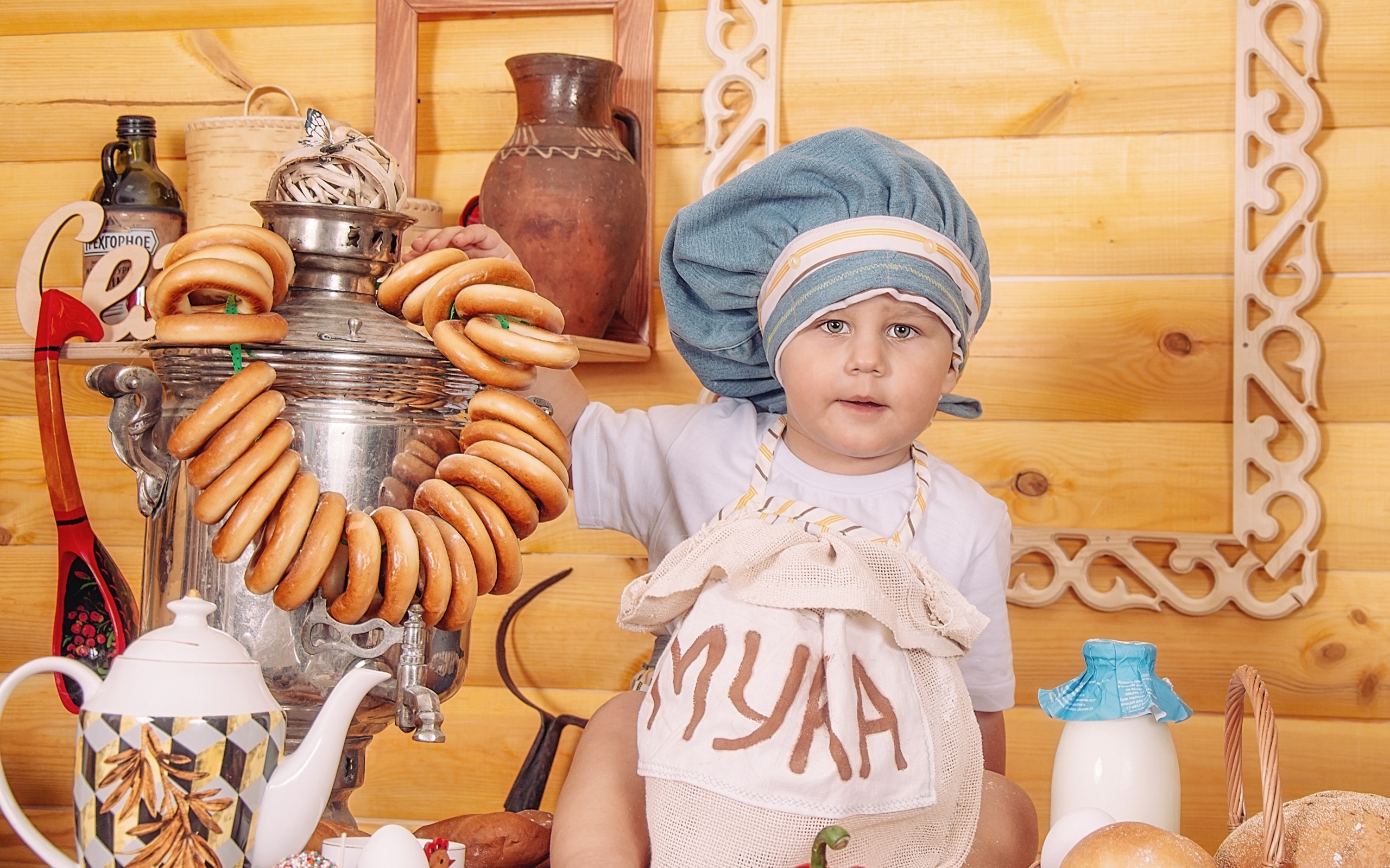 Маленький мальчик повар с продуктами и самоваром на столе