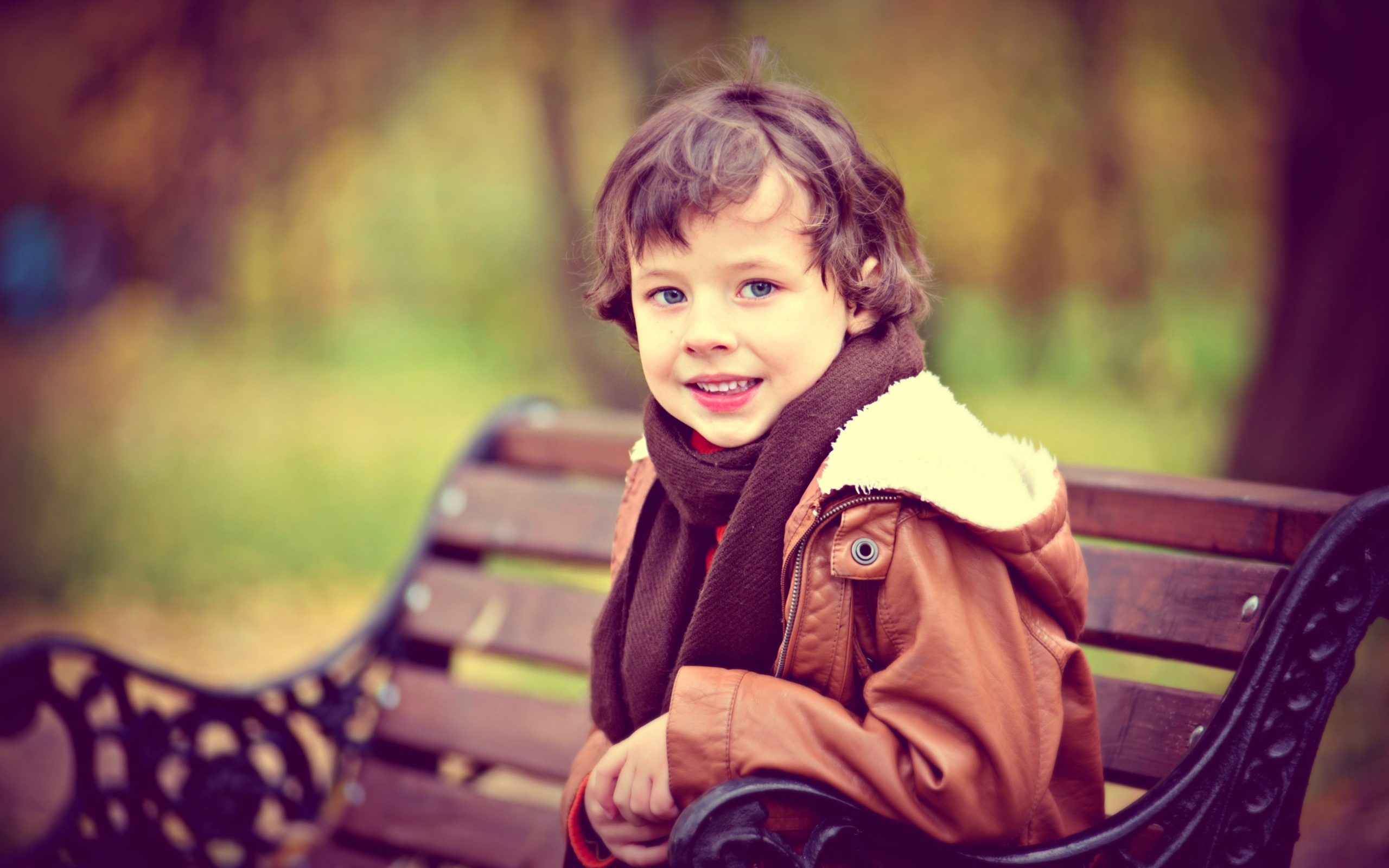 Маленький улыбающийся мальчик на лавке в парке