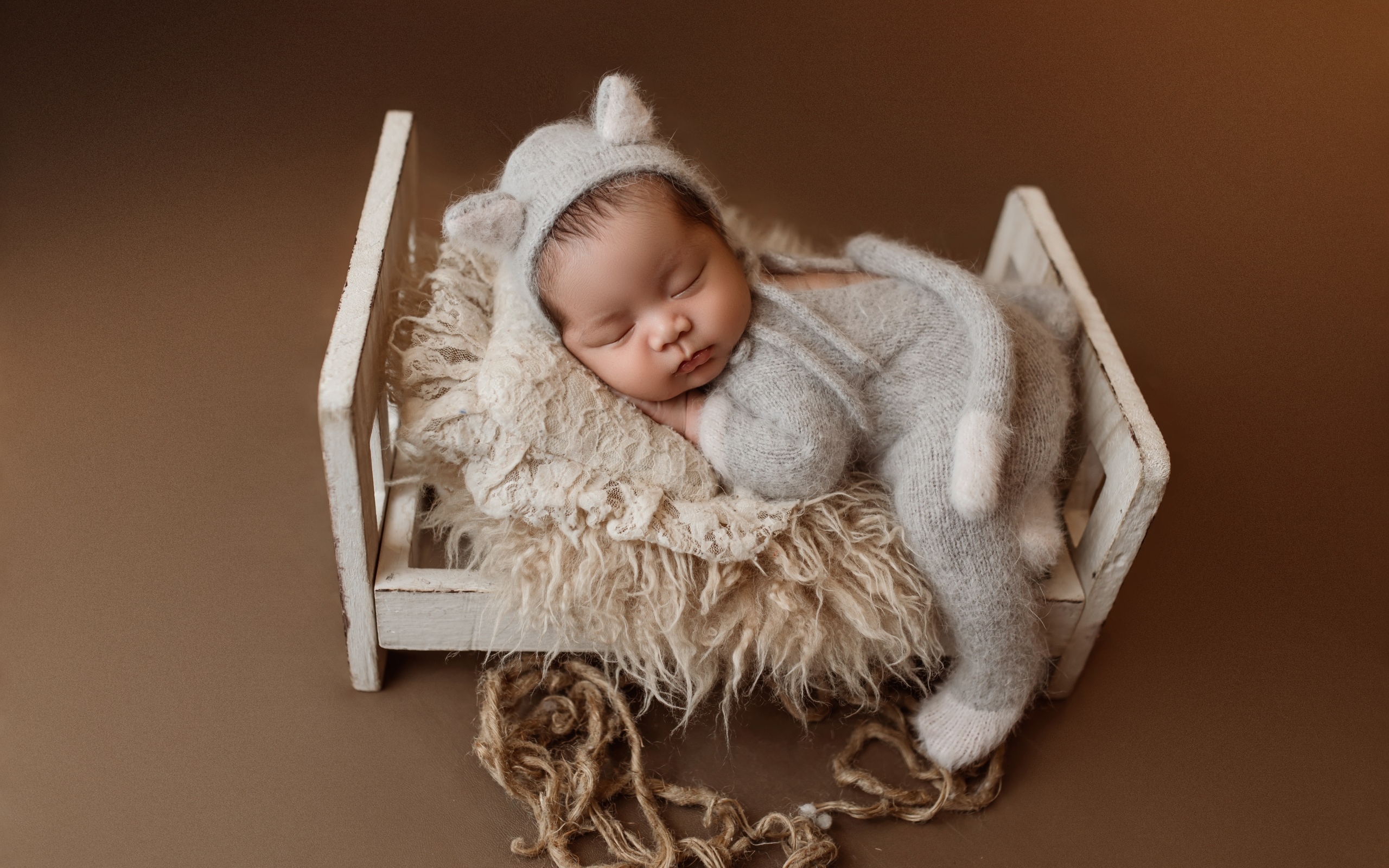 Спящий ребенок на маленькой кровати на коричневом фоне