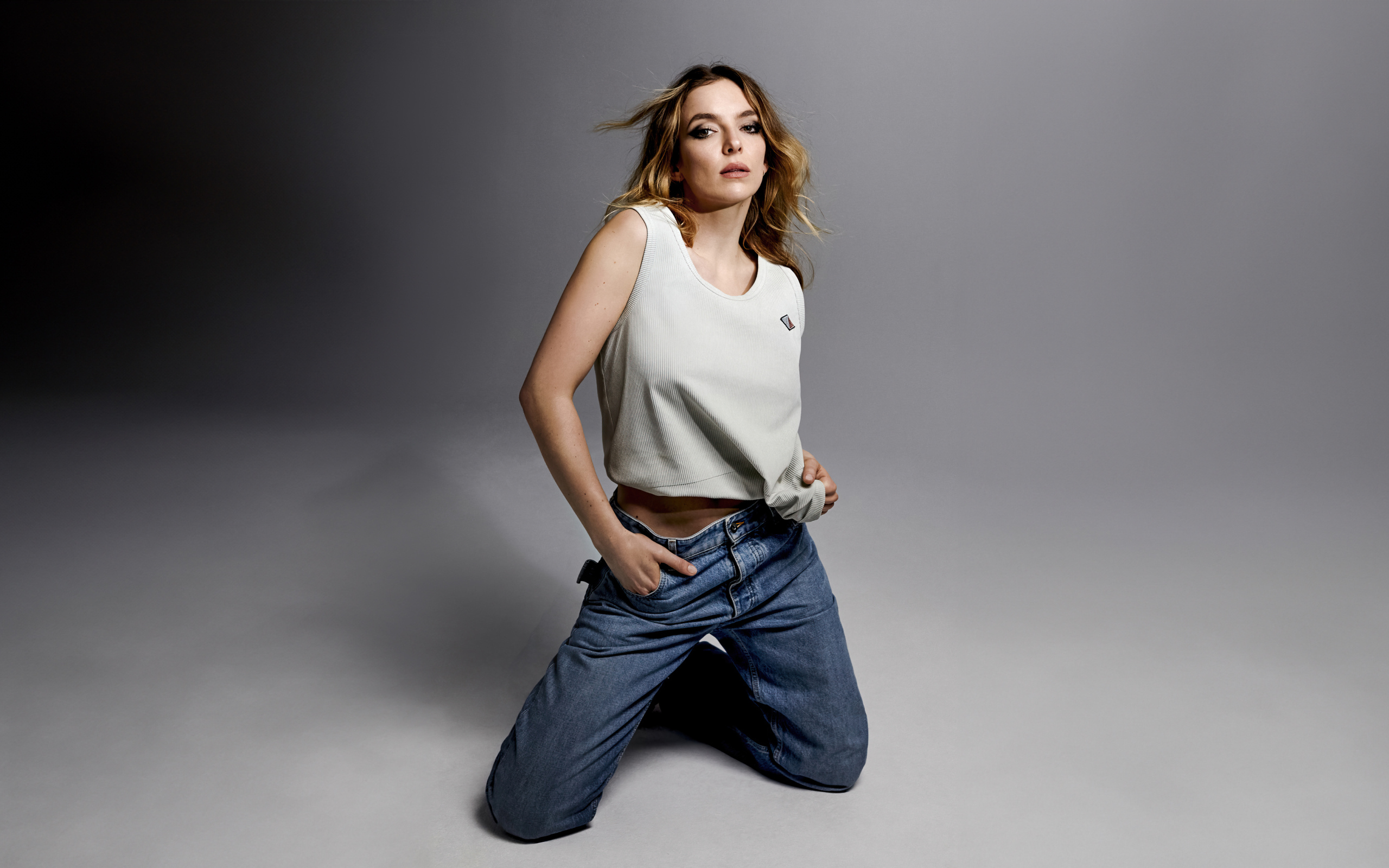 Британская актриса Джоди Комер в джинсах на сером фоне