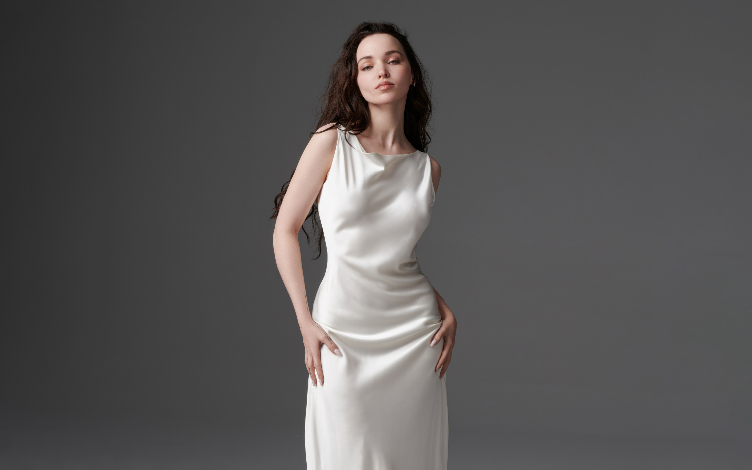 Стройная девушка актриса Дав Кэмерон в белом платье на сером фоне