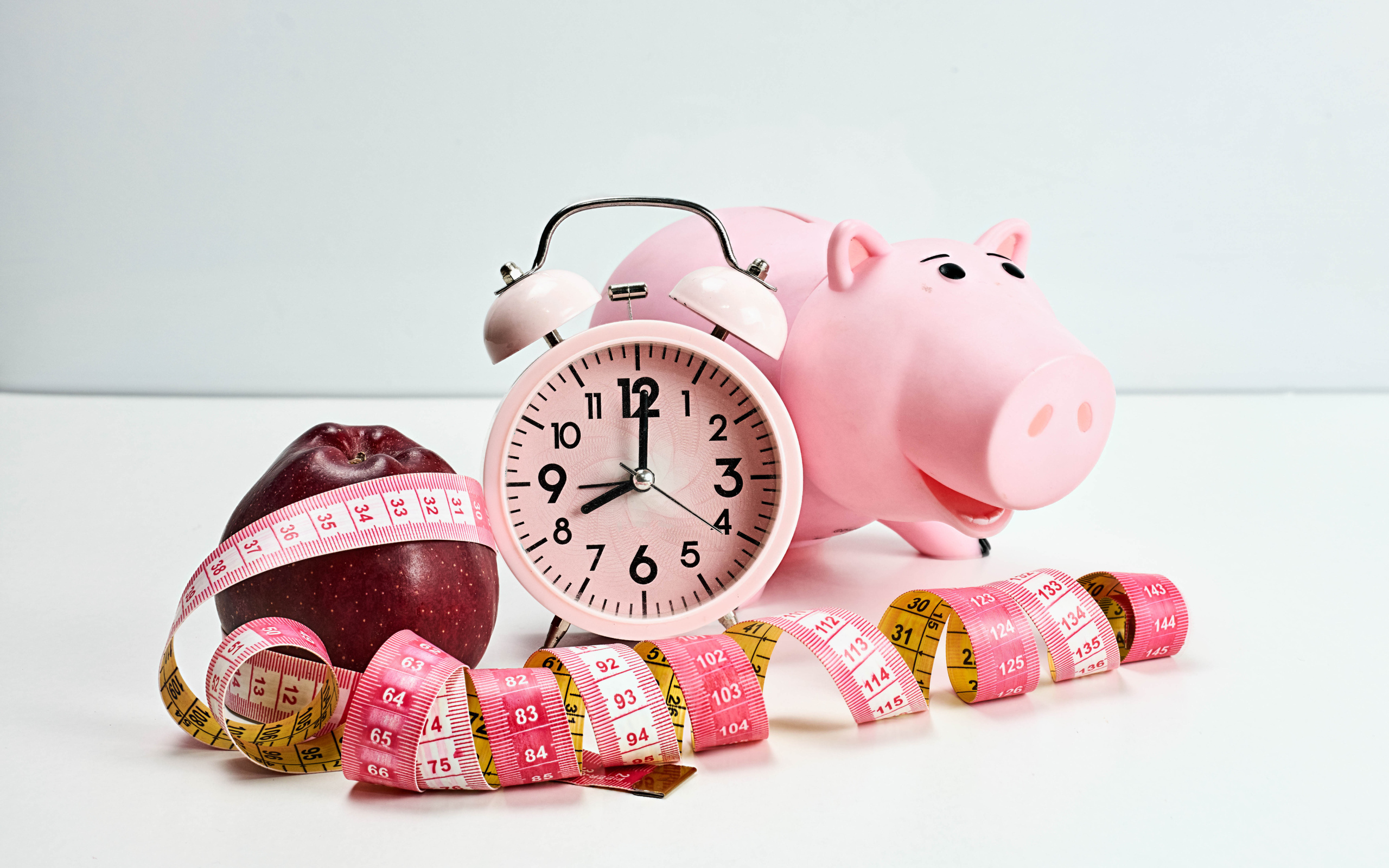 Мерная лента, яблоко, будильник и свинья копилка на белом фоне