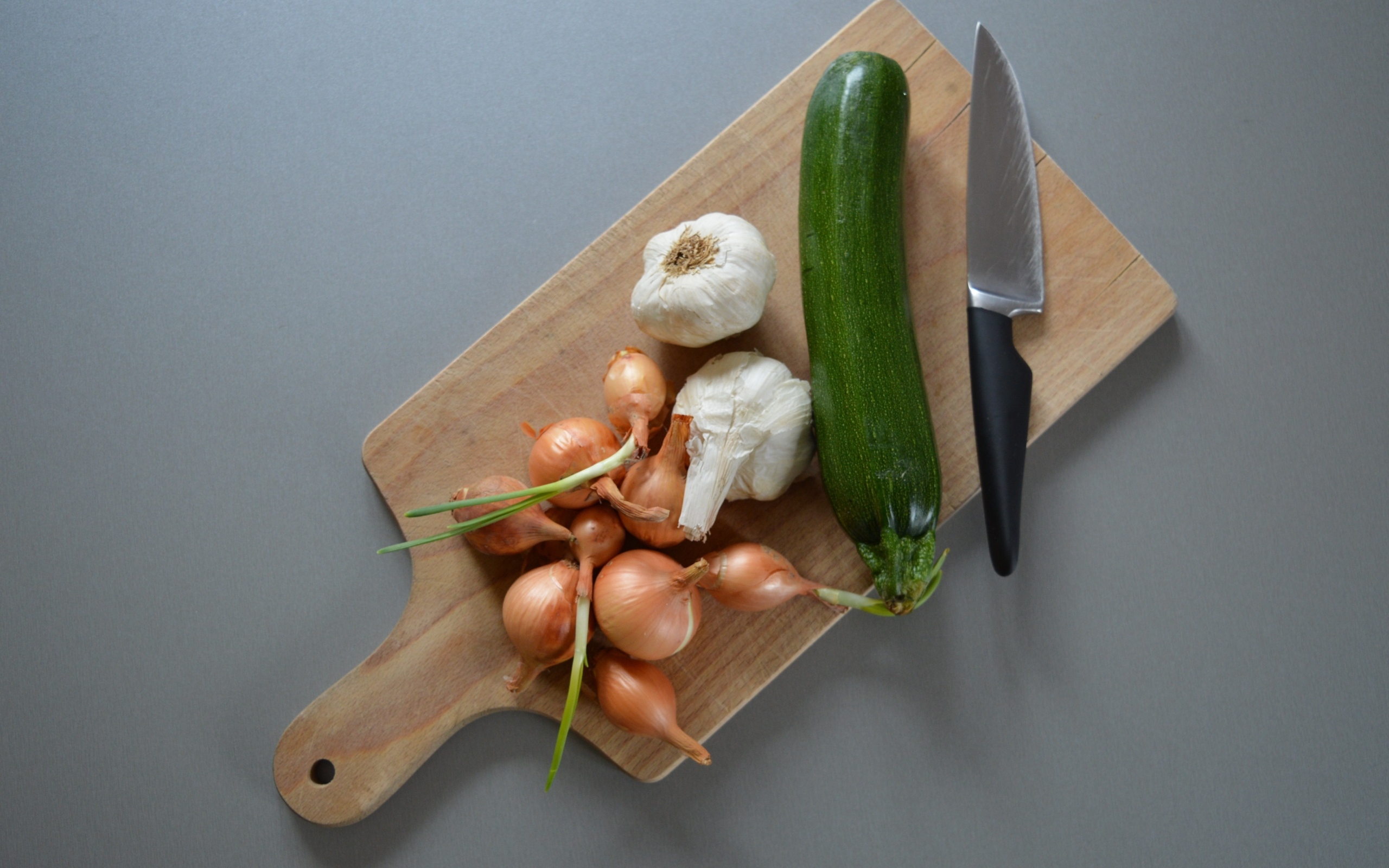 Лук, чеснок и кабачок на разделочной доске с ножом