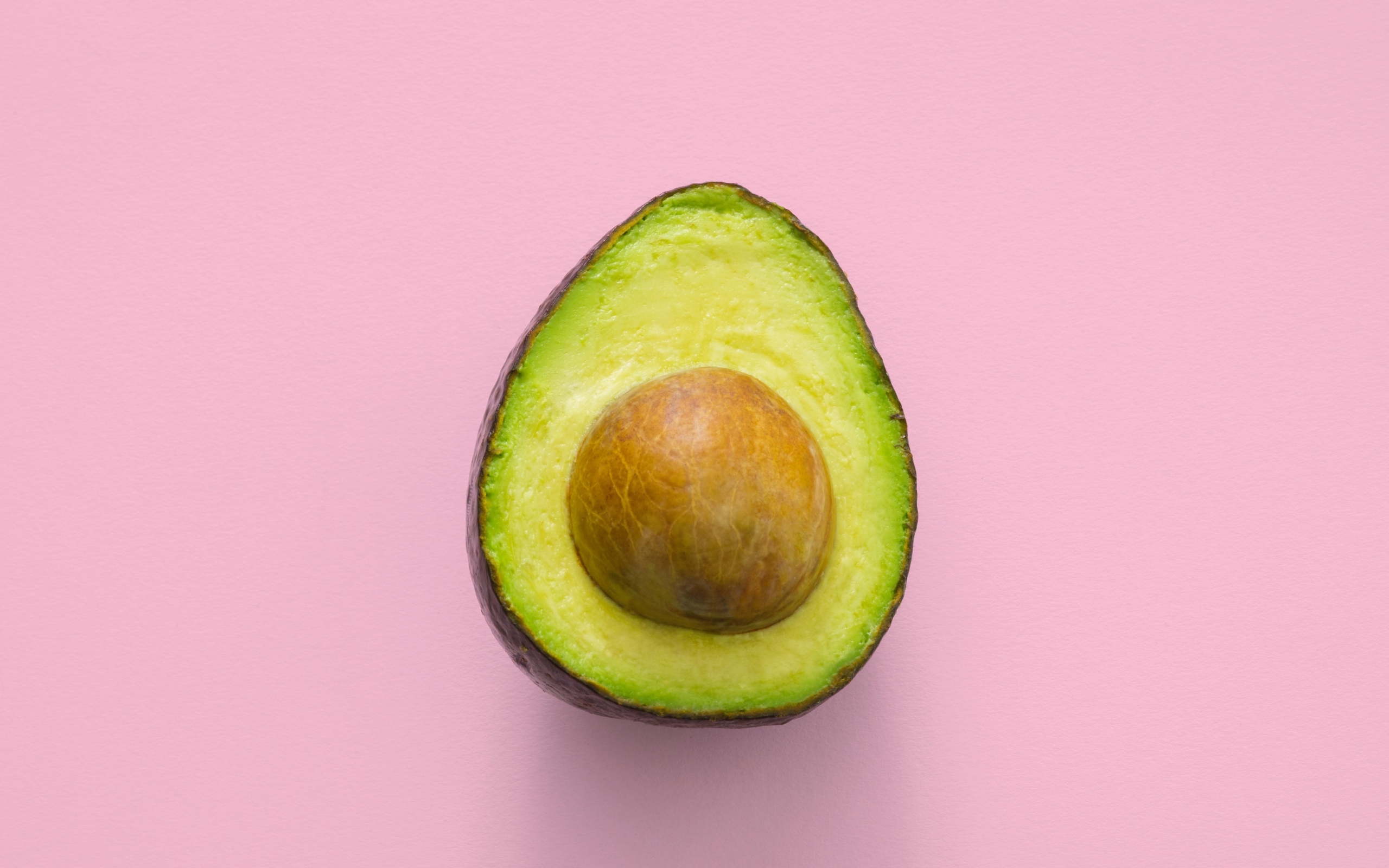 Половина авокадо с большой косточкой на розовом фоне