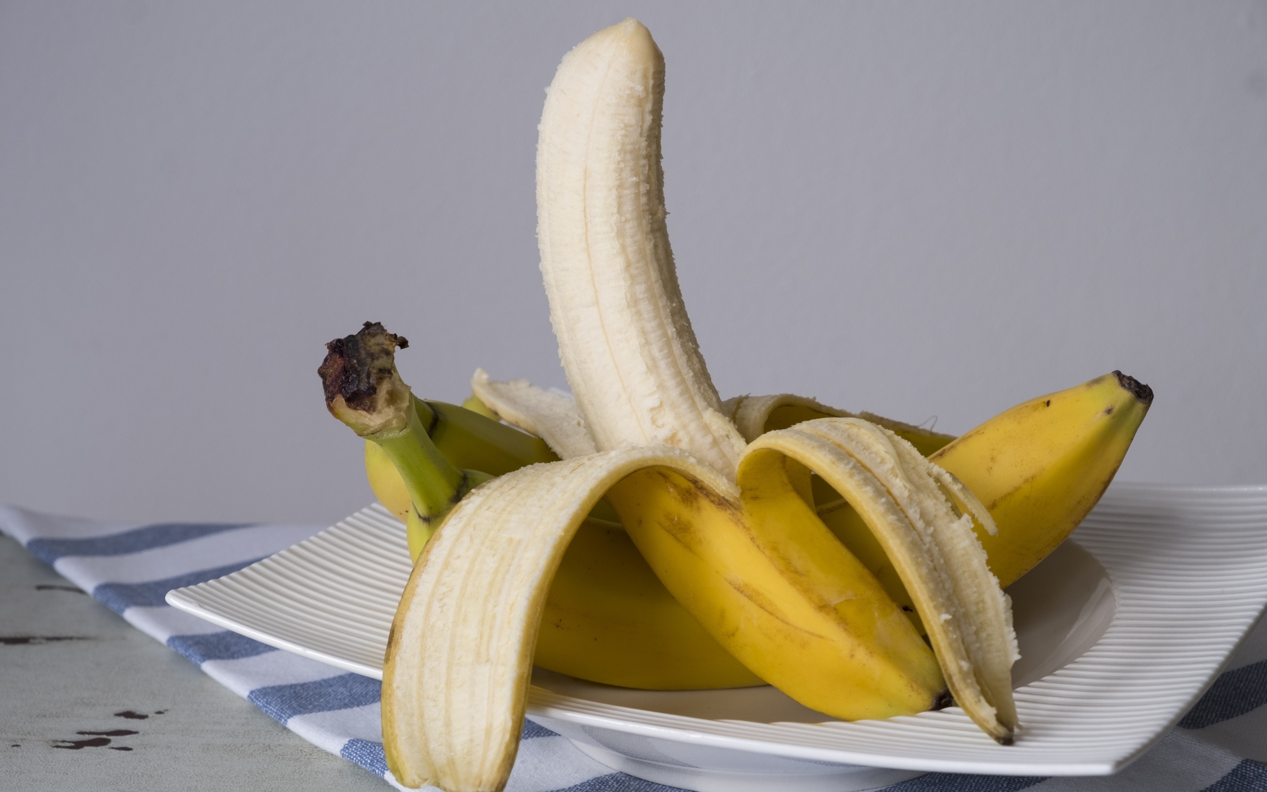 Очищенный банан на тарелке на сером фоне