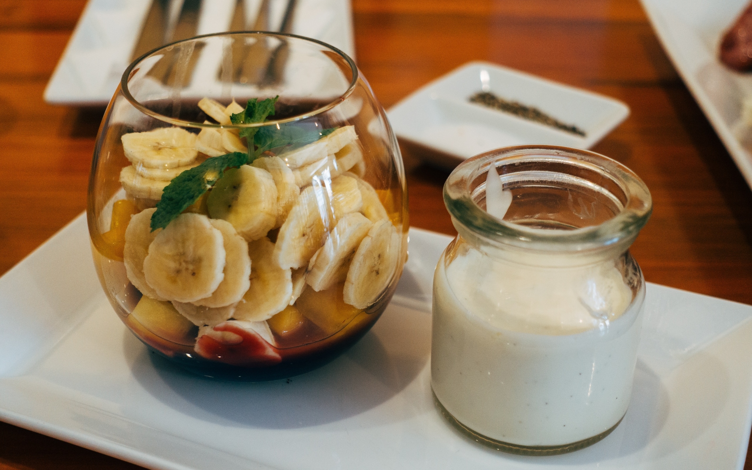 Нарезанные бананы в стакане на столе с йогуртом