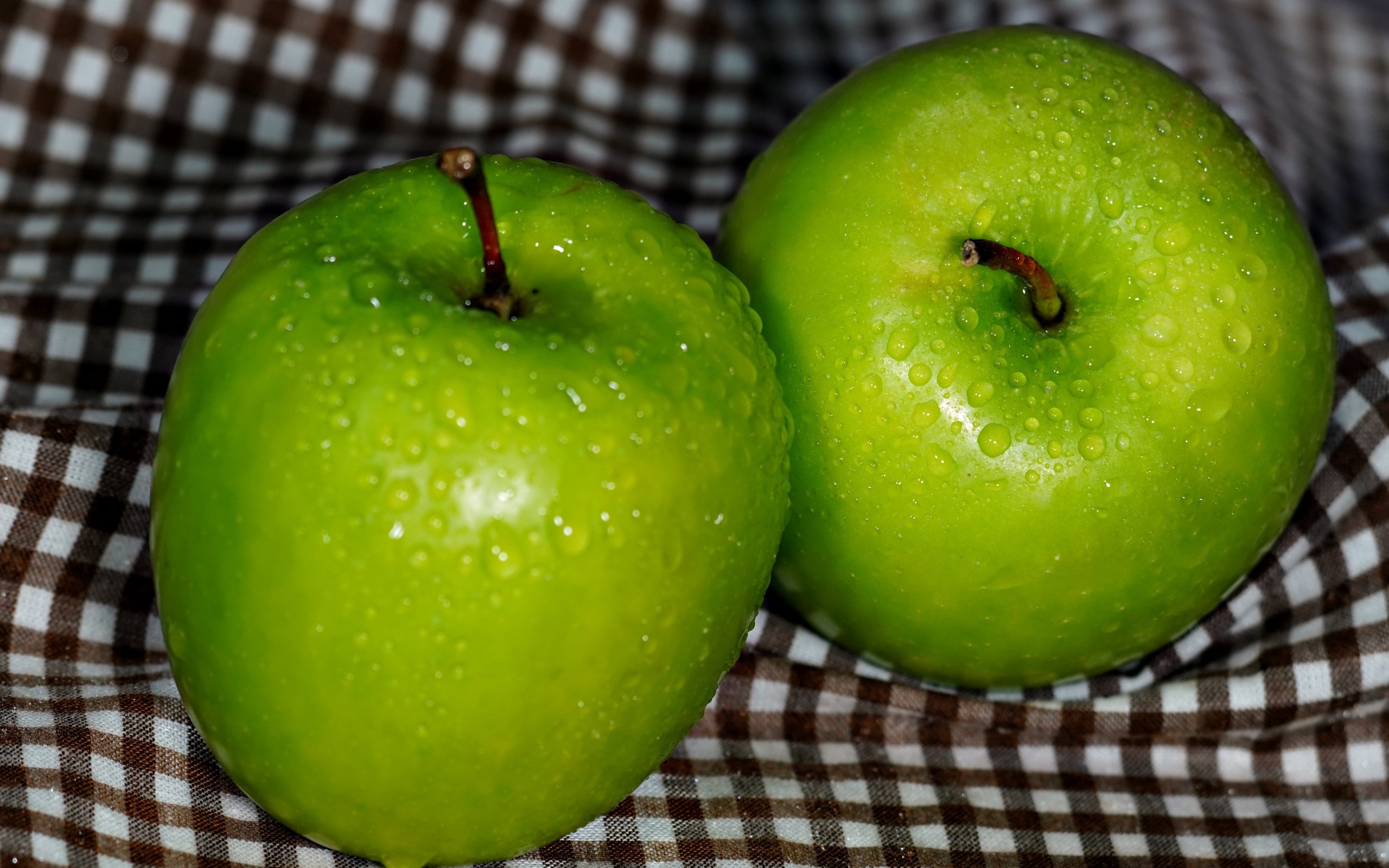 Два мокрых зеленых яблока на скатерти