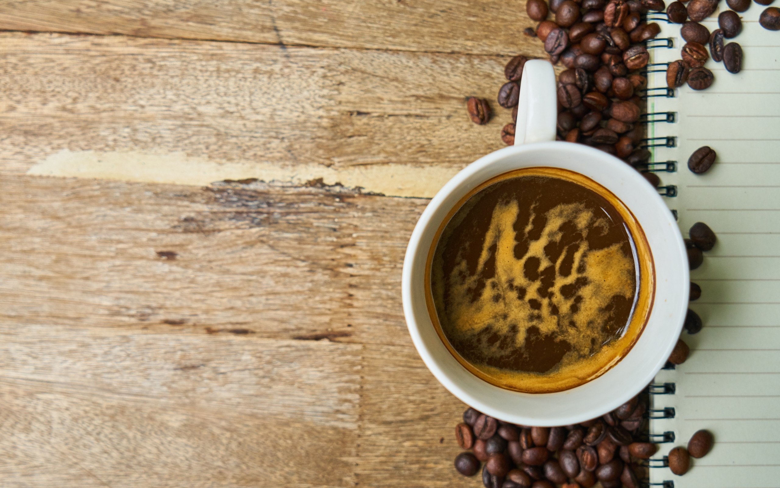 Чашка кофе с кофейными зернами и блокнотом на столе