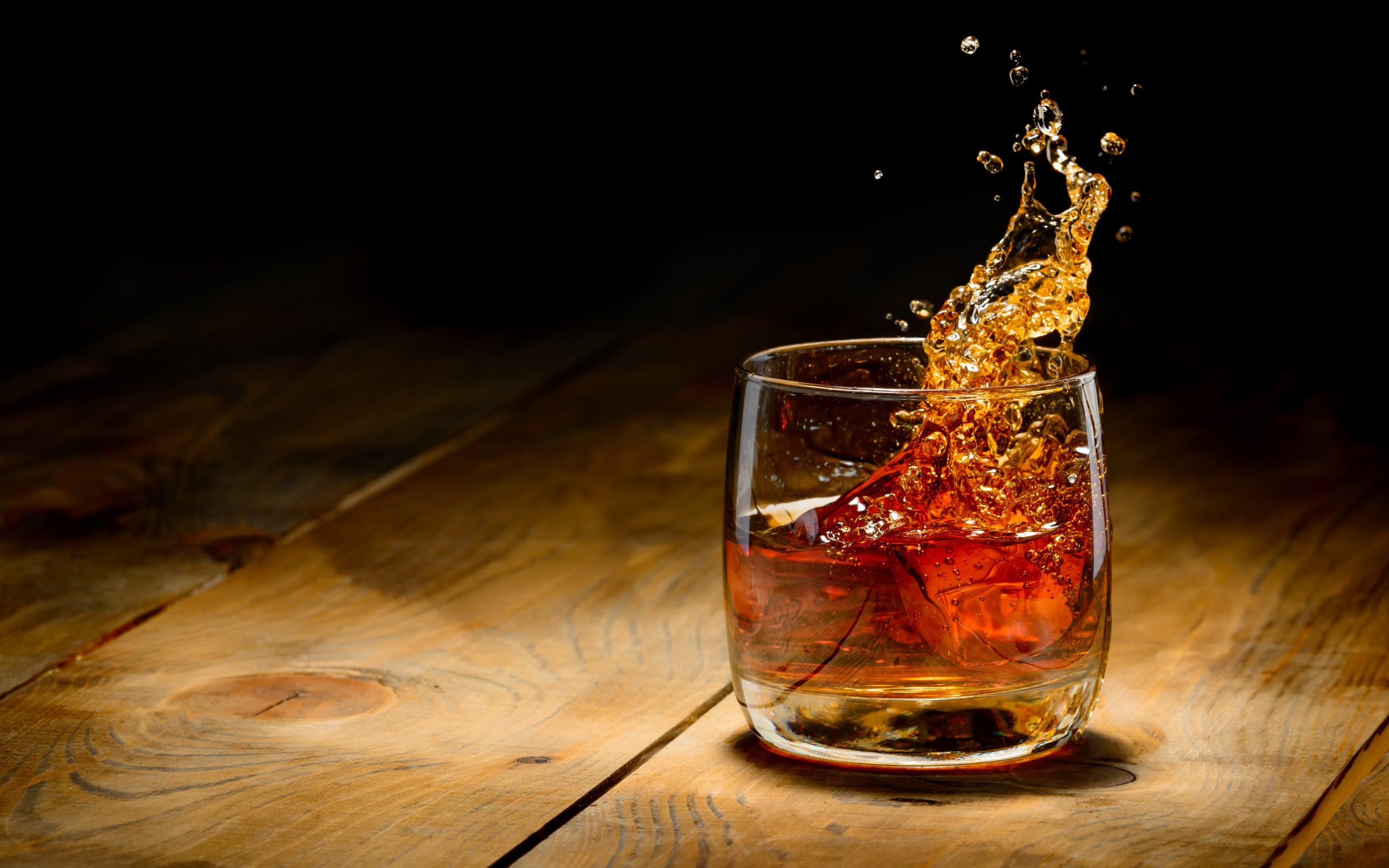 Брызги в стакане с виски со льдом на столе