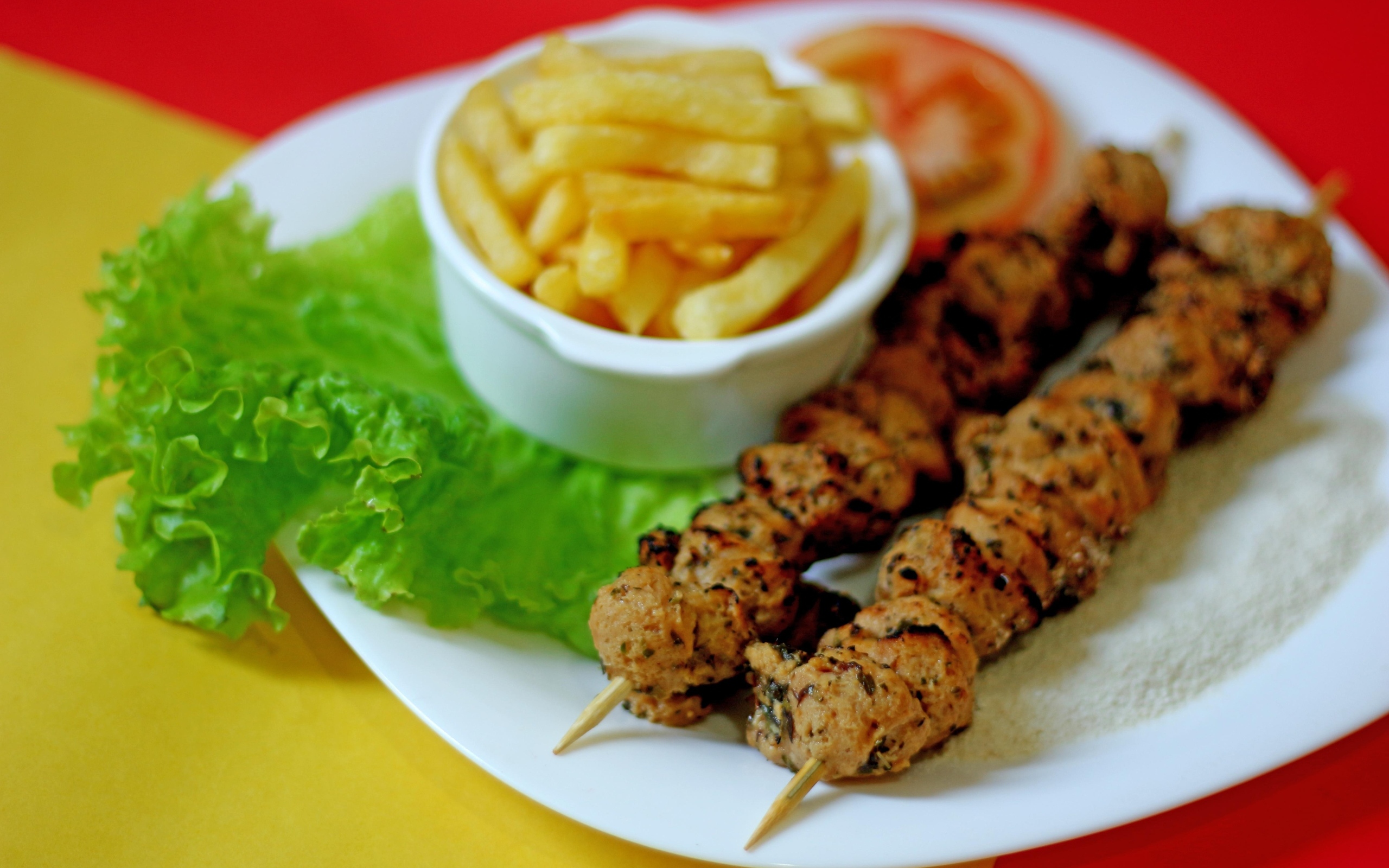 Шашлык на шпажках на столе с картофелем фри и листьями салата