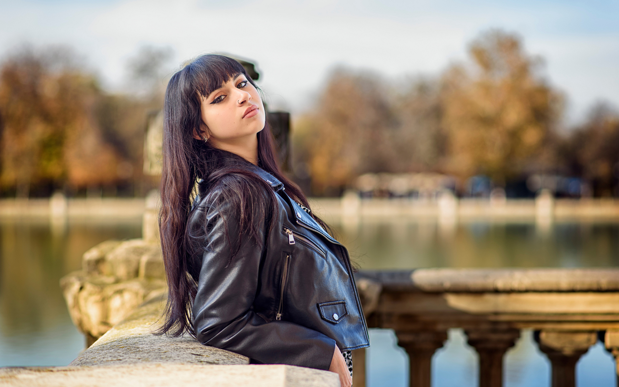 Девушка в черной куртке стоит на мосту у воды