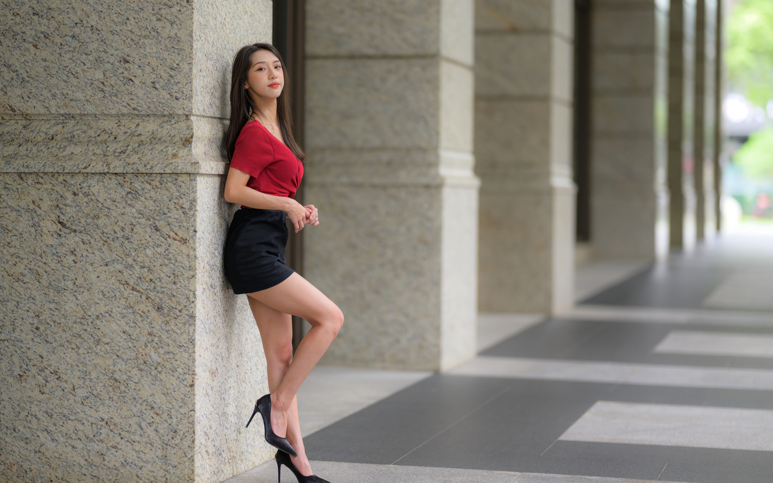 Азиатка в короткой черной юбке стоит у стены