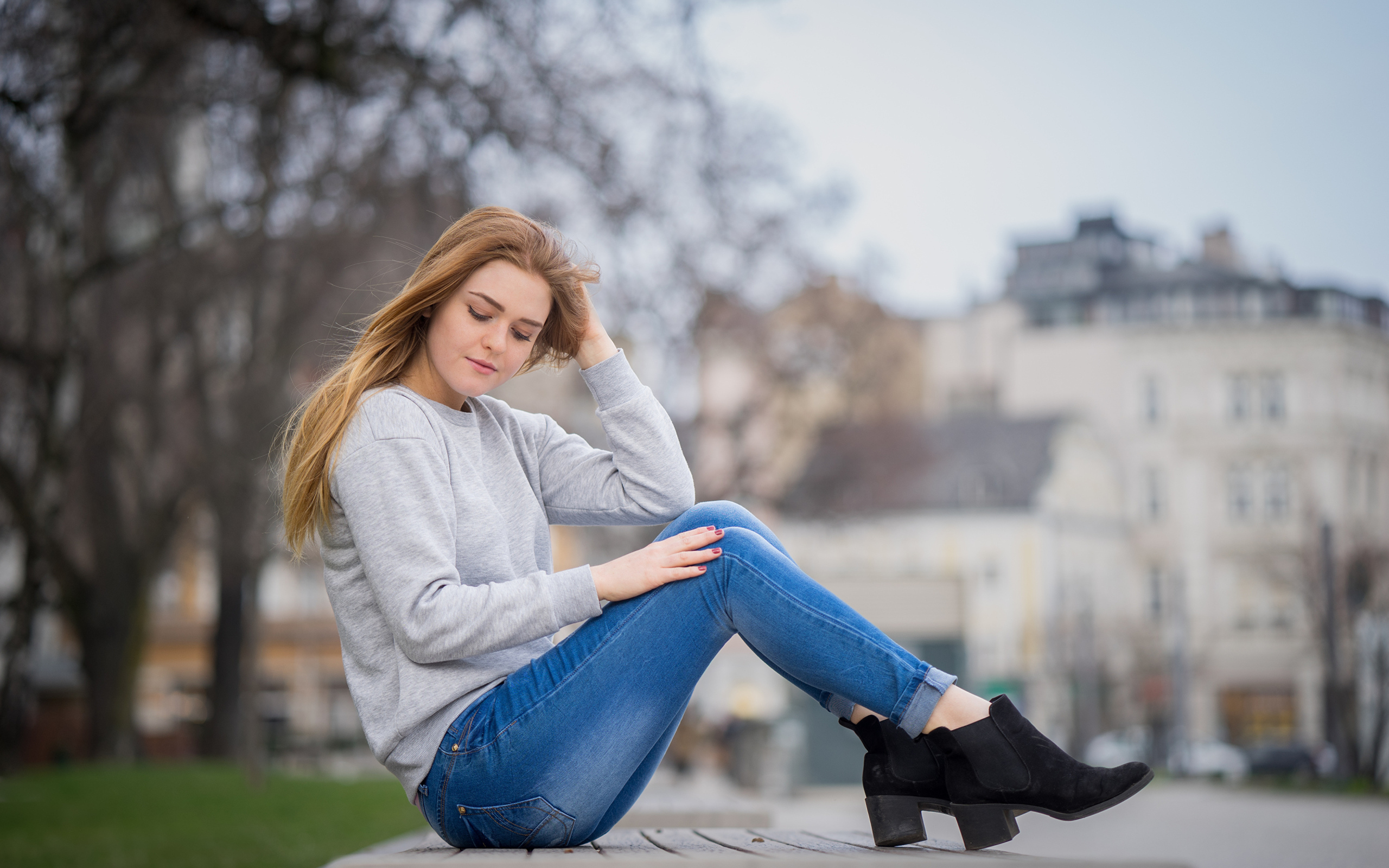 Милая девушка в синих джинсах сидит на лавке