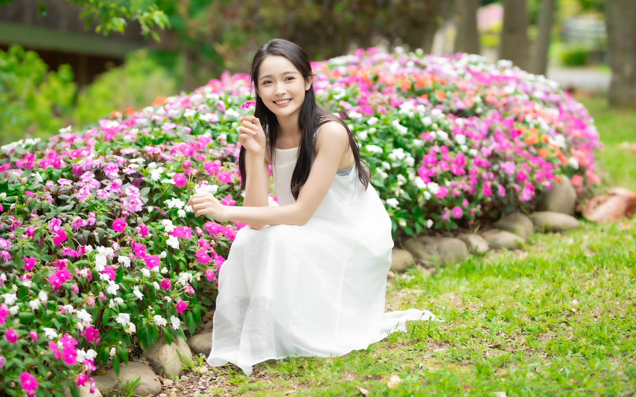 Милая улыбающаяся азиатка в белом платье сидит у цветов