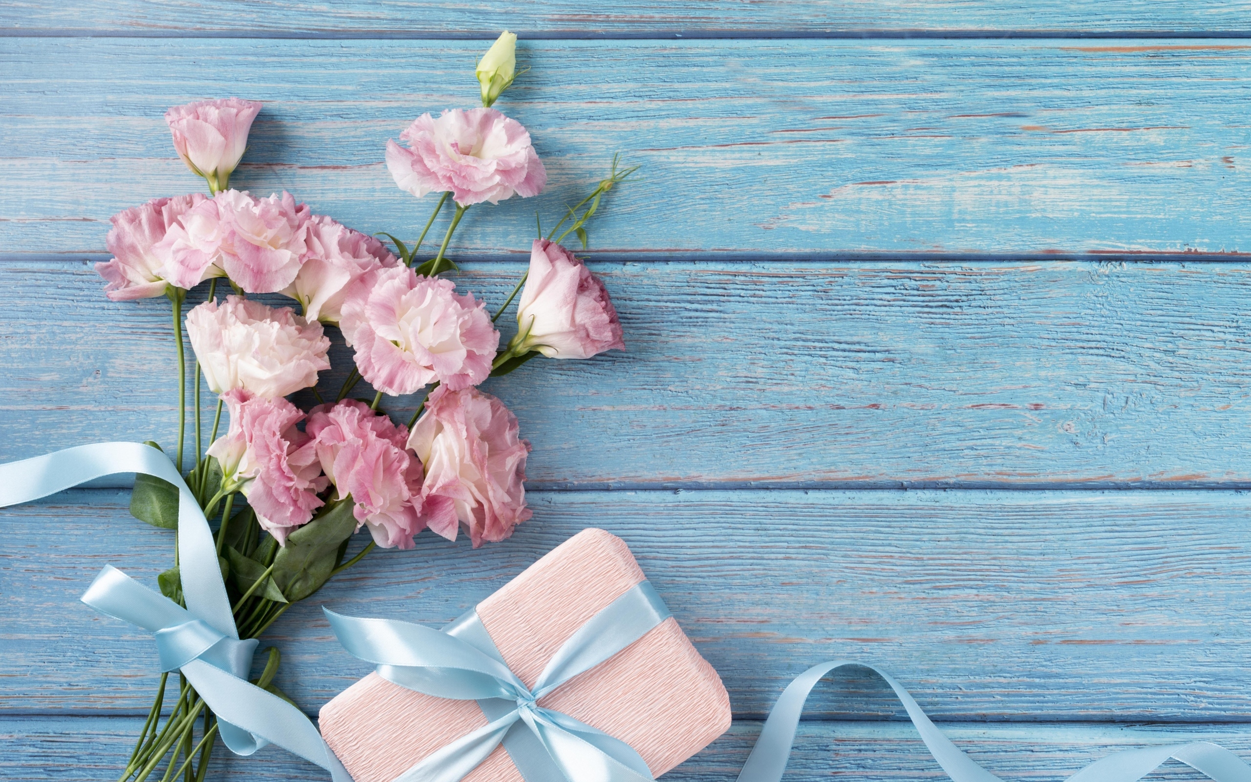 Букет розовых цветов эустомы с подарком на голубом столе