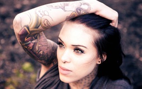 Девушка брюнетка с пирсингом в носу и татуировкой на руке