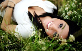 Brunette girl with piercing in the nose lies in the grass