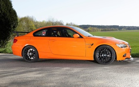 Оранжевый BMW M3 GTS на фоне зеленого поля