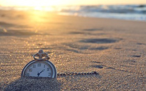 Часы на цепочке лежат в песке