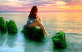Русалка на зеленых камнях смотрит на закат