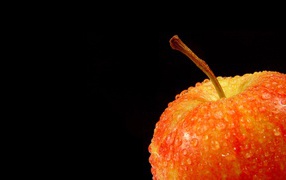 Влажное оранжевое яблоко на черном фоне