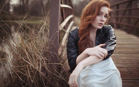 Девушка в кожаной куртке сидит у деревянного моста