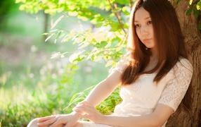 Азиатская девушка прислонилась спиной к дереву