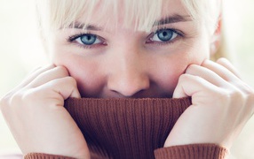 Blonde girl hides her face in the collar sweater