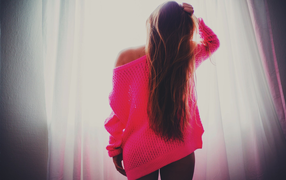 Брюнетка в розовой кофте стоит у окна