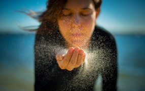 Девушка сдувает песок с руки