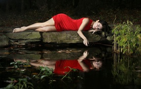 Girl in red dress lies on a stone at the pond