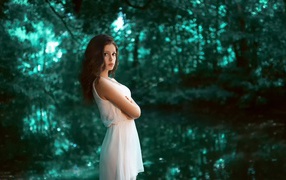 Девушка в белом платье стоит в зеленом лесу