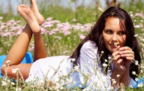 Девушка лежит на животе и держит в руке белый цветок