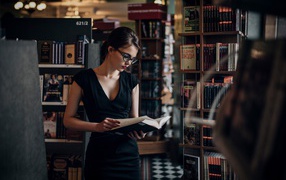Девушка читает среди книжных полок