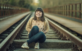 Девушка улыбается сидя на рельсах