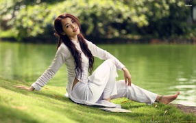 Японская девушка в белом костюме сидит на берегу водоема