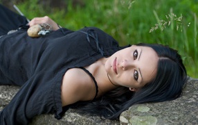 Модель в черном платье лежит на камне в траве