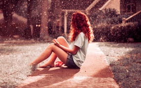 Red-haired girl sitting on the ground in the rain