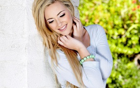 Улыбающаяся блондинка прислонилась к белой стене