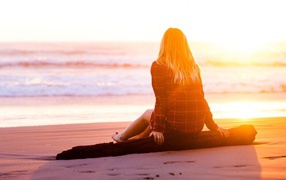 Девушка на сидит на пляже во время заката