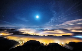 Night city in the valley under the cover of fog