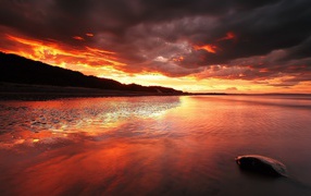 Stone in shallow water on a background of red sunset