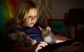 Девочка играет с планшетом лежа в кровати