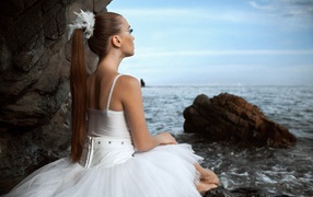 A ballerina in a white dress sitting on the beach
