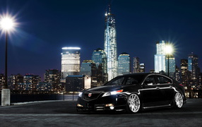 Черный автомобиль Acura TL на фоне ночных небоскребов 